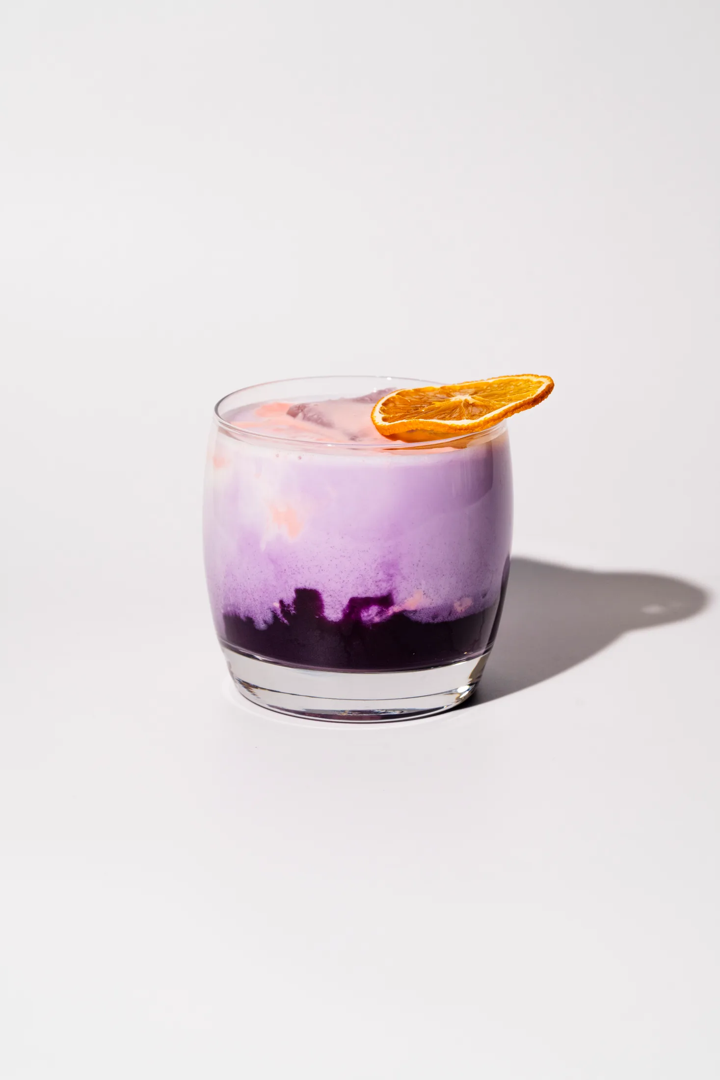 An orange ube latte in a short glass on white