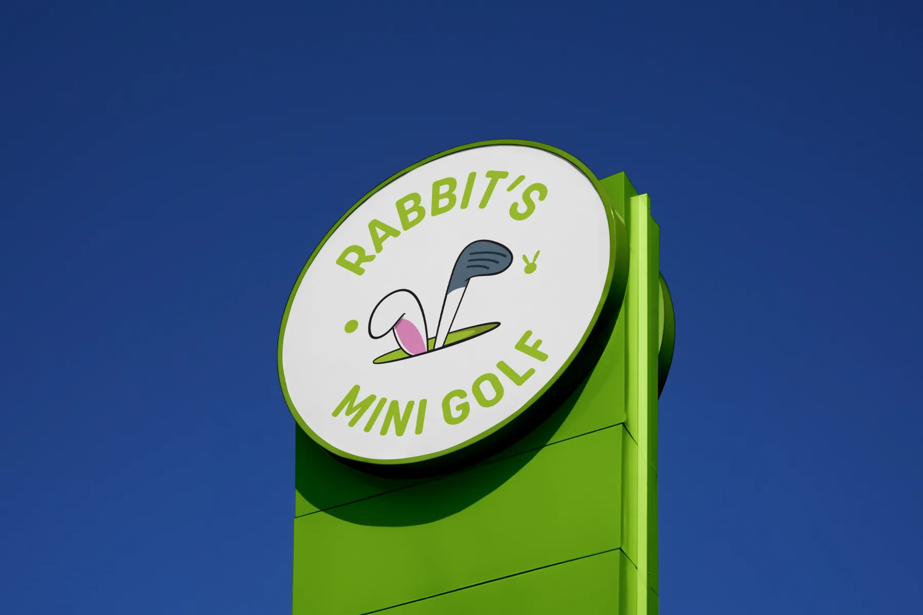 The round green and white Rabbit’s Mini Golf pylon sign against a deep blue sky