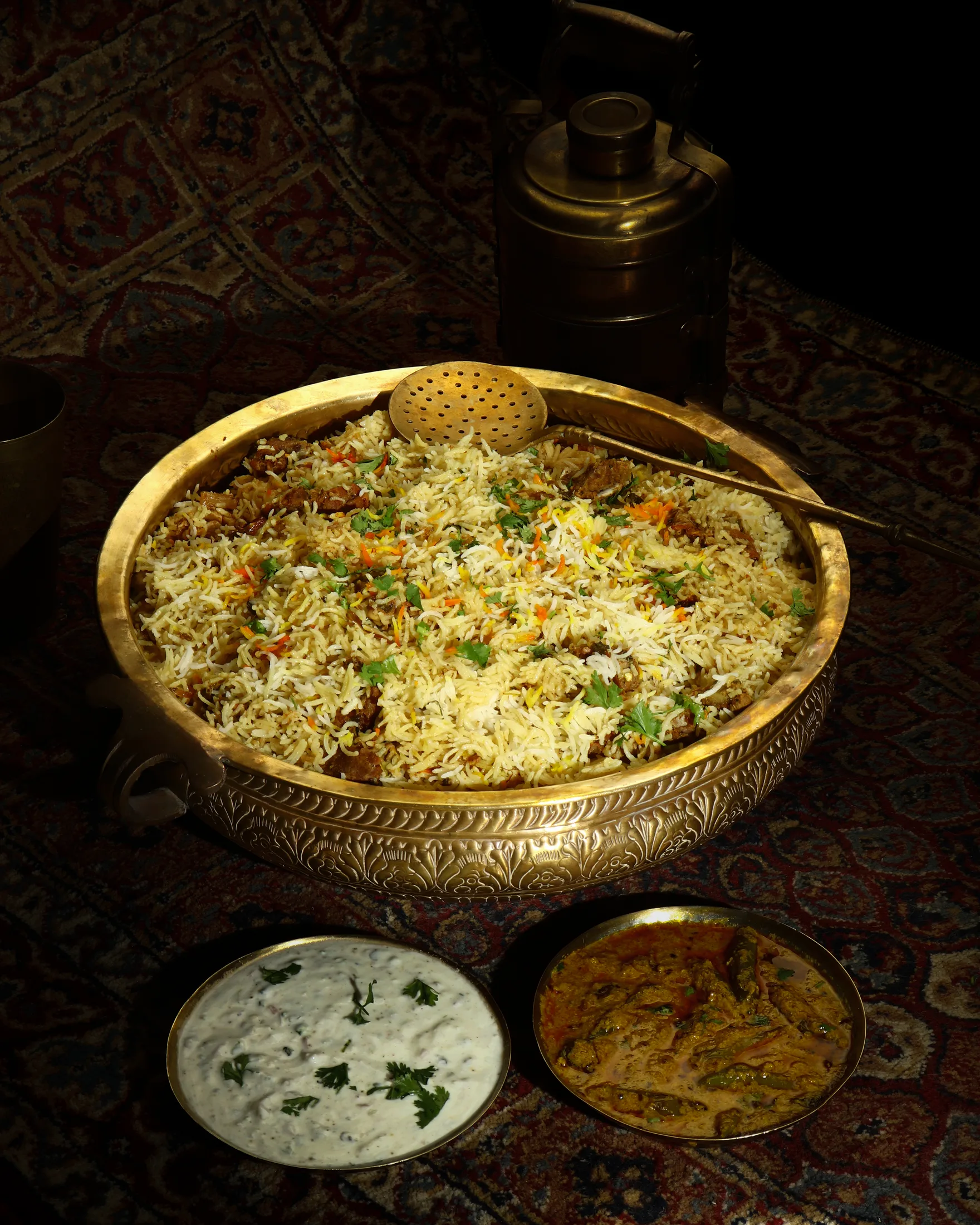 Mutton biryani in a brass bowl with raita and curry